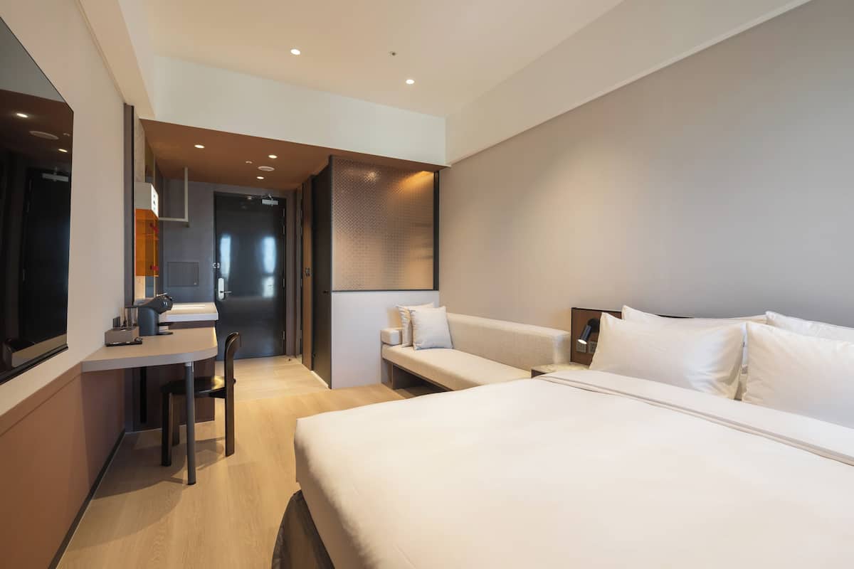 A modern hotel room with a bed, a desk, and a seating area.