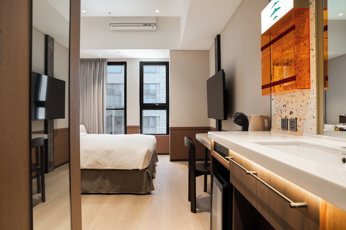 Una habitación de hotel moderna con cama, televisión, escritorio con silla y baño con espejo y lavamanos.
