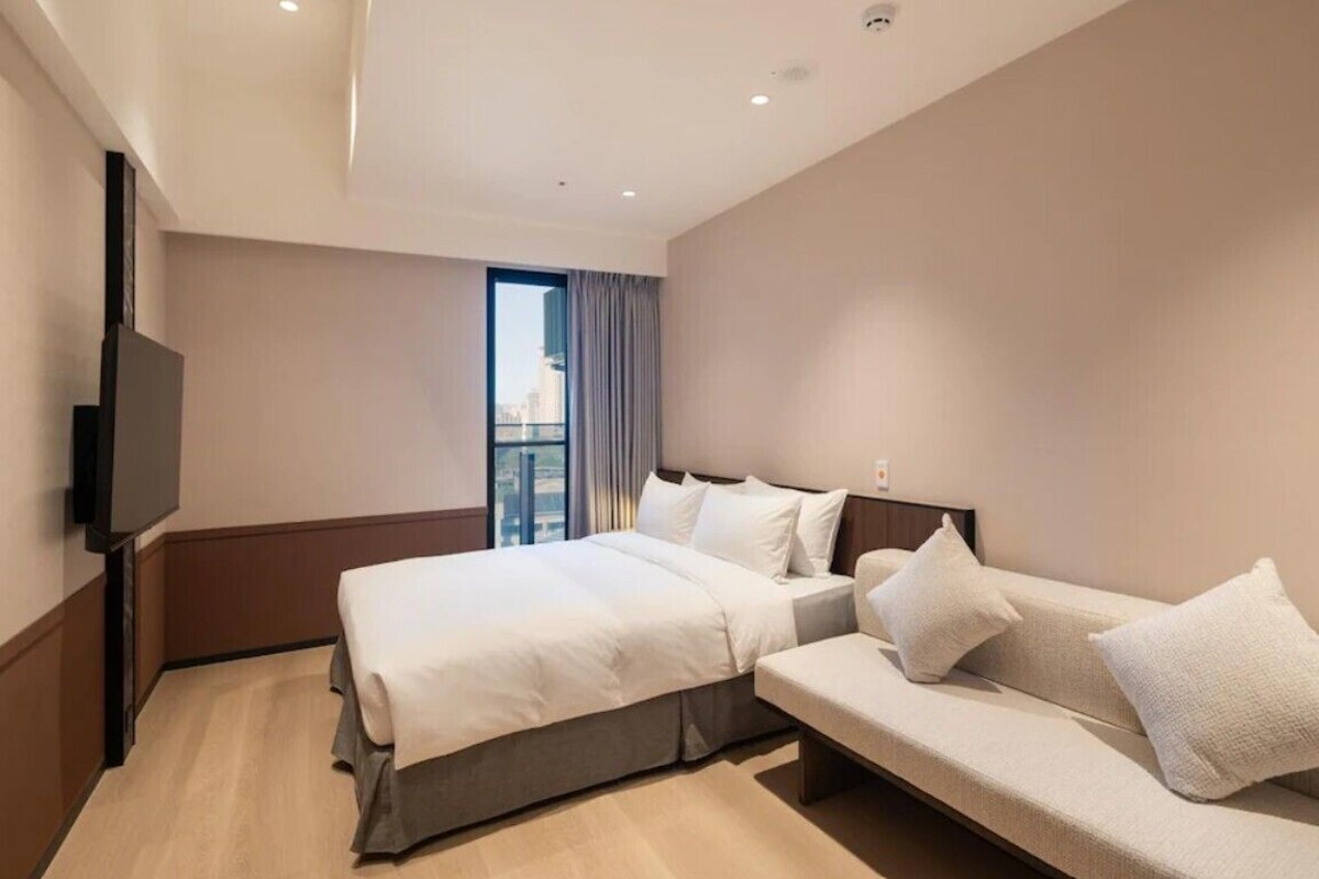 Habitación de hotel con cama, sofá, televisión y ventana con cortinas.