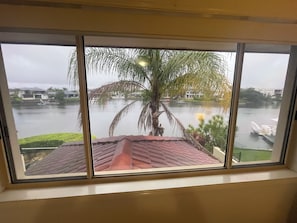 A view through a window with a view of a body of water, a palm tree, and a building across the water. - Beach House on the Gold Coast Canal - Room 3 (Helensvale)