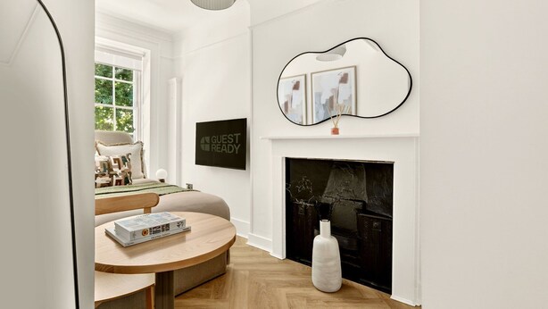 A modern living room with a fireplace, a round table with a book, a sofa, and a wall-mounted artwork. - GuestReady - Comfortable Double Room in London (London)