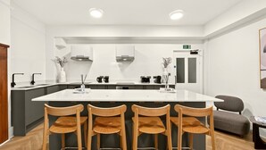 A modern kitchen with a central island, bar stools, and a seating area with a grey sofa. - GuestReady - Comfortable Double Room in London (London)