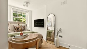 Une chambre moderne avec un lit, une table ronde en bois, un miroir et une pancarte indiquant « PRÊT POUR LES INVITÉS ».