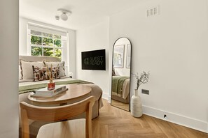A modern bedroom with a bed, a round wooden table, a mirror, and a 'GUEST READY' sign. - GuestReady - Stylish Double Room in Central London (London)