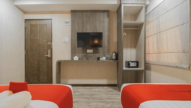 A hotel room with a wooden reception desk, a television, a coffee machine, and two beds with red headboards. - Paragon Nagoya Hotel Batam (Batam)