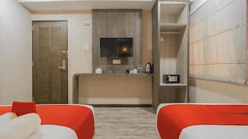 Una camera d'albergo con una reception in legno, una televisione, una macchina per il caffè e due letti con testiere rosse.