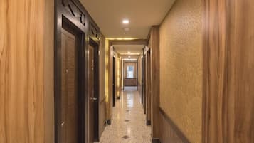 Un corridoio d'hotel con pannelli in legno, un pavimento in marmo lucido e una serie di porte.