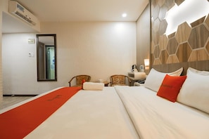 A hotel room with a large bed, two chairs, a small table, and a mirror.
