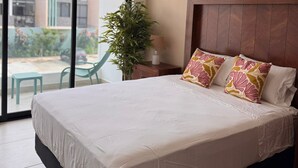 Ein Hotelzimmer mit Bett, Nachttisch, Lampe, einer Zimmerpflanze und Blick ins Freie.
