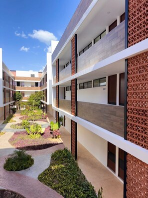 Un immeuble moderne à plusieurs étages, doté d’une cour intérieure agrémentée de jardins paysagers et d’un chemin en briques.