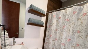 Ein Badezimmer mit weißem Waschbecken, Toilette, einer Duschvorhang mit Blumenmuster und zwei Ablagen über der Toilette.