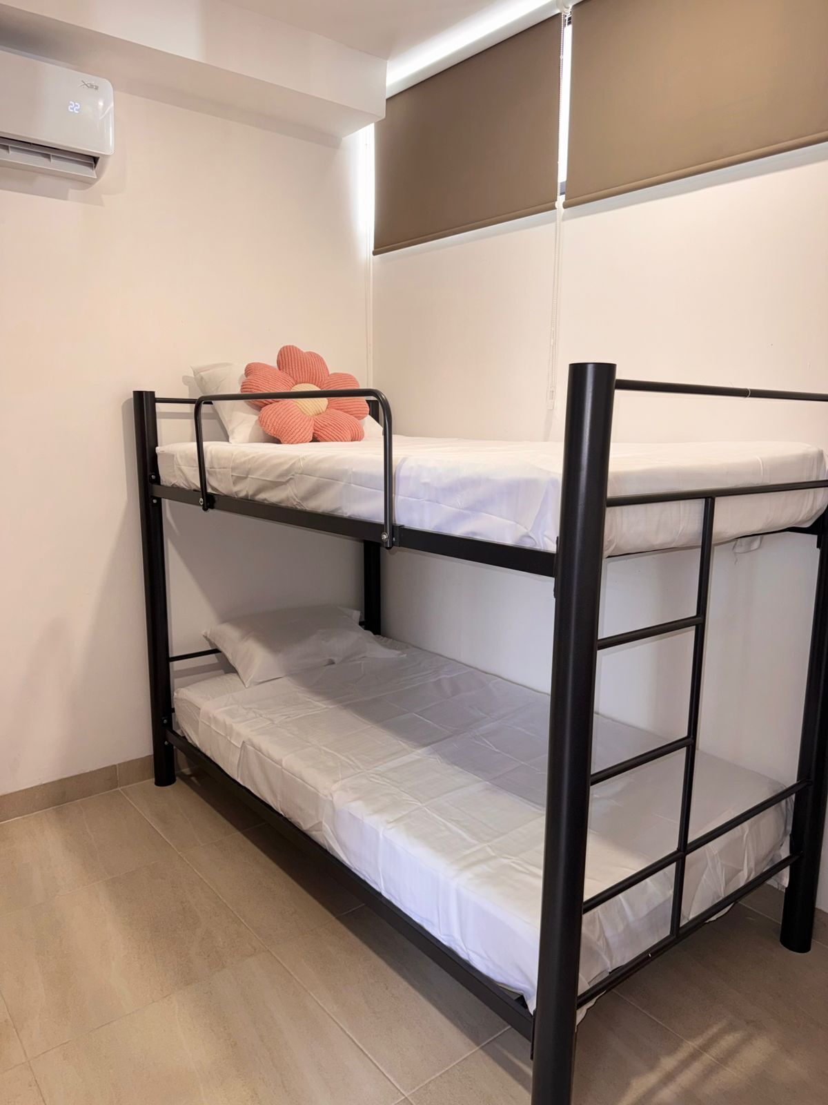 Een stapelbed met een witte matras, een onderste bed met een wit kussen, en een bovenste bed met een roze kussen.