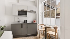 Een moderne keuken met grijze kastjes, een ingebouwde magnetron en een koffieapparaat. Er is een eethoek met een ronde tafel en twee stoelen.