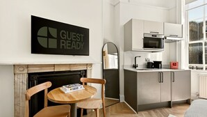 Ett modernt kök med mikrovågsugn, ugn och kaffebryggare, en öppen spis och en skylt med texten ”KLART FÖR GÄSTER”.