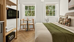 Et gæsteværelse med en seng, to vinduer, et fjernsyn, et skrivebord og en stol.
