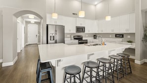 Une cuisine moderne avec des meubles blancs, des appareils en acier inoxydable et un îlot central doté de tabourets de bar.