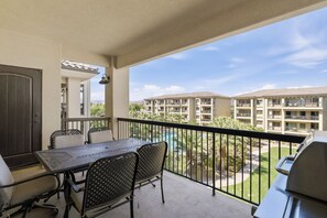 A balcony with a table and chairs, a grill, and a view of a pool and buildings. - Estancia Resort | Pool + Hot Tub + Near Trails (St. George)