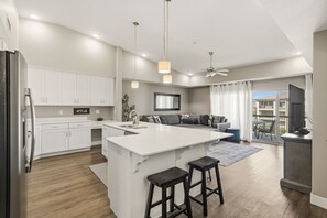 A modern kitchen with white cabinets, a central island, and a dining area with a sofa. - Estancia Resort | Pool + Hot Tub + Near Trails (St. George)