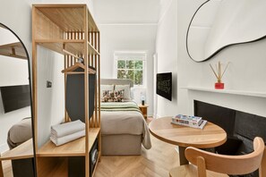 A compact room with a bed, a small table, a chair, a bookshelf, and a fireplace. - GuestReady - Modern Double Room near King's Cross (London)