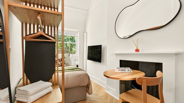 Una camera moderna con un letto a castello, un tavolo rotondo in legno, una sedia, un camino e una TV che mostra il messaggio 'GUEST READY'.
