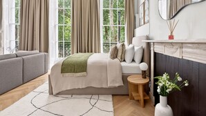 Une chambre à coucher avec un lit, un canapé, une petite table, un vase de fleurs et une cheminée.
