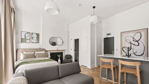 Une chambre d’hôtel moderne équipée d’un lit, d’un canapé, d’un bureau avec des chaises, d’une cheminée et d’œuvres d’art accrochées aux murs.