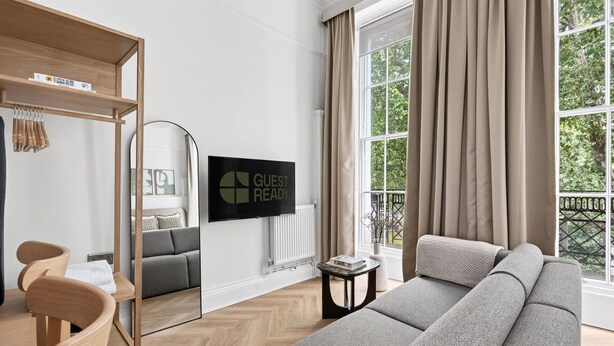 Un salon moderne comprenant un canapé, un bureau, une chaise, un téléviseur et une fenêtre avec des rideaux.