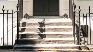 Une porte noire avec une flèche verte au-dessus, une pancarte indiquant « PRÊT POUR LES CLIENTS » sur la droite, et un escalier menant à l’entrée.