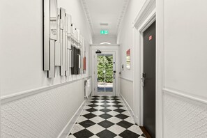 A hallway with a checkered floor, white walls, and a door with a red sign. - GuestReady - Bright Double En-Suite near Euston (London)