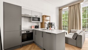 Een moderne keuken met grijze kastjes, een magnetron en een inbouwoven. Er is een grijze bank en een raam met gordijnen.