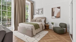 Een slaapkamer met een groot raam, een bed, een stoel en kunstwerken aan de wanden.