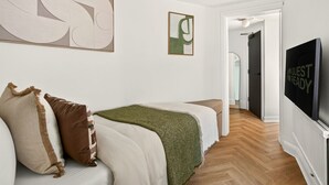 Ein Hotelzimmer mit einem Bett, einem Fernseher und einem Gang zu einem weiteren Zimmer.