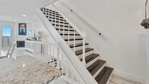Eine Treppe mit weißen Geländern und Holzstufen, die zu einer Empfangshalle mit einem weißen Schrank und einem Gemälde führt.