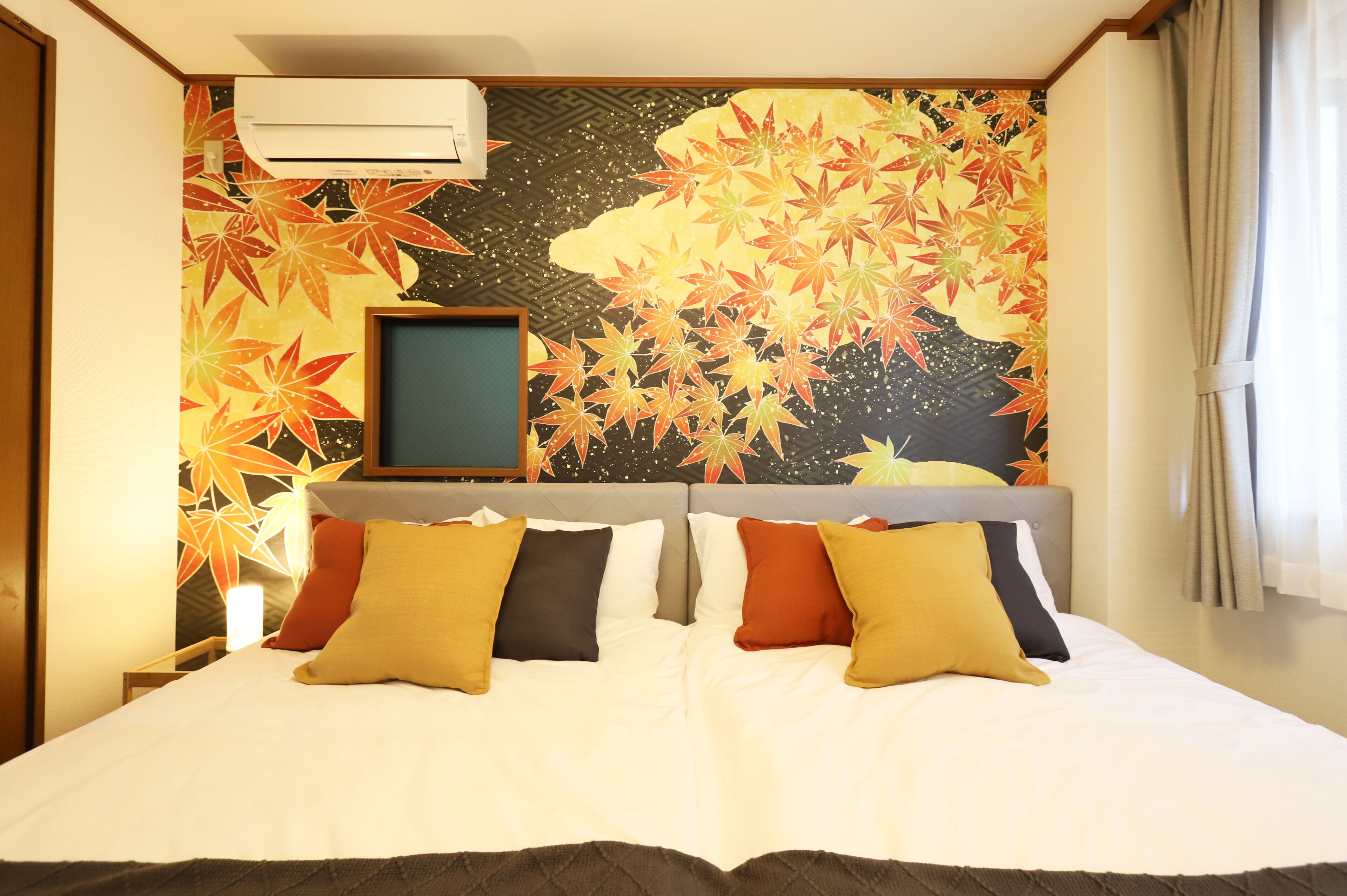 A hotel room with a bed, pillows, a television, and a wall with a leaf pattern.