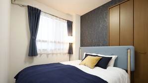 Een netjes opgemaakt bed met een blauw hoofdeinde, een raam met gordijnen en een houten garderobe.