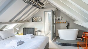Ett modernt hotellrum med en stor säng, en rymlig klädkammare, ett badkar och ett ljust, sluttande tak.