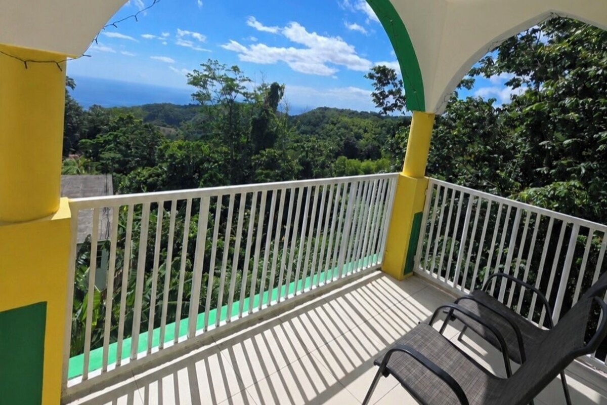 Un balcón con barandilla blanca, vistas a un paisaje verde y cielo despejado.