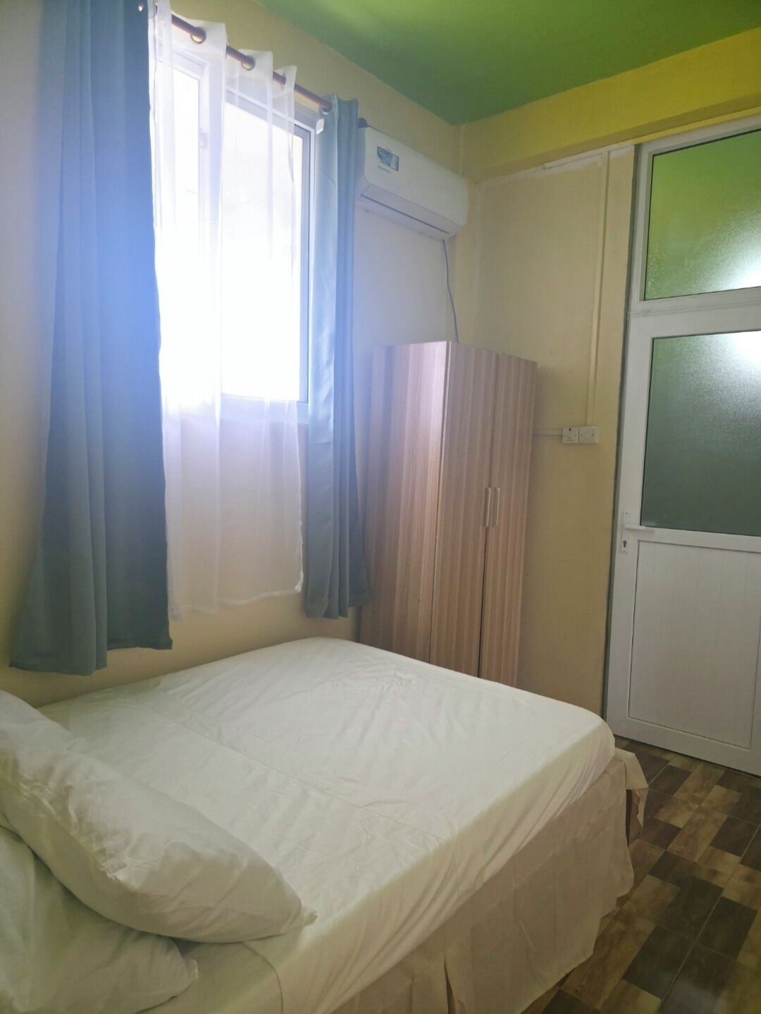 Ein Zimmer mit einem Bett, einem Kleiderschrank, einem Fenster mit Vorhängen und einer Tür.