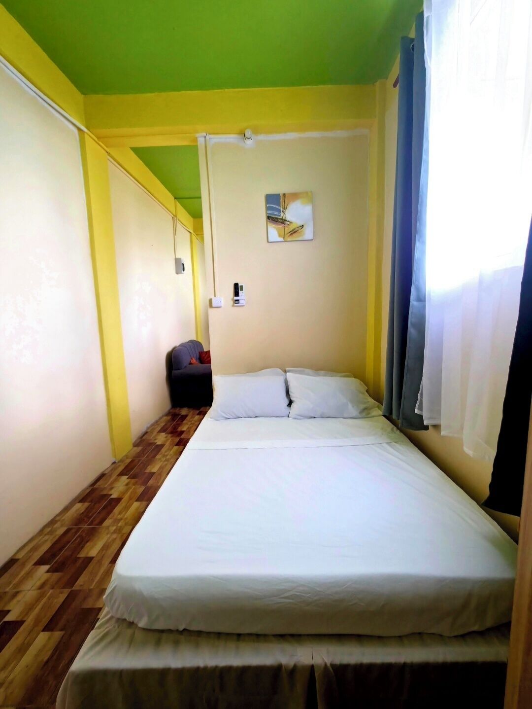 Una habitación pequeña con cama individual, piso de madera, techo verde y un cuadro en la pared.