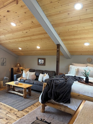 A cozy room with a wooden ceiling, a sofa, a bed, and a small table.