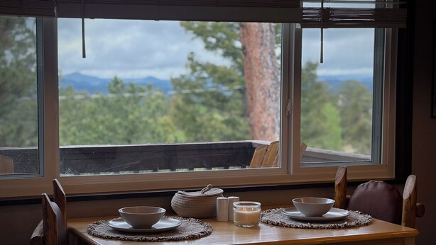 A dining table with two bowls and a candle, set against a window with a view of trees and mountains. - The Perch Point Studio- Peaceful getaway in Florrisant (Florissant)