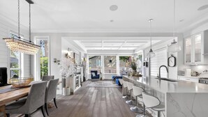 A modern kitchen with a marble countertop, a built-in sink, and a dining area with a wooden table and bar stools. - Luxury 4BR | Steps to Beach, Hot Tub & Theatre (Surrey)