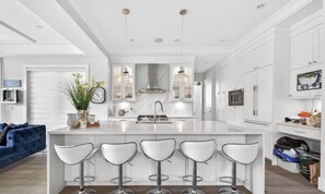 A modern kitchen with a central island, bar stools, pendant lighting, and a built-in oven. - Luxury 4BR | Steps to Beach, Hot Tub & Theatre (Surrey)