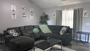Un salon moderne avec un canapé d’angle, une table basse, un ventilateur de plafond et une plante en pot.