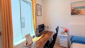 A bedroom with a bed, a desk with a computer, a chair, a window with curtains, and a painting on the wall.