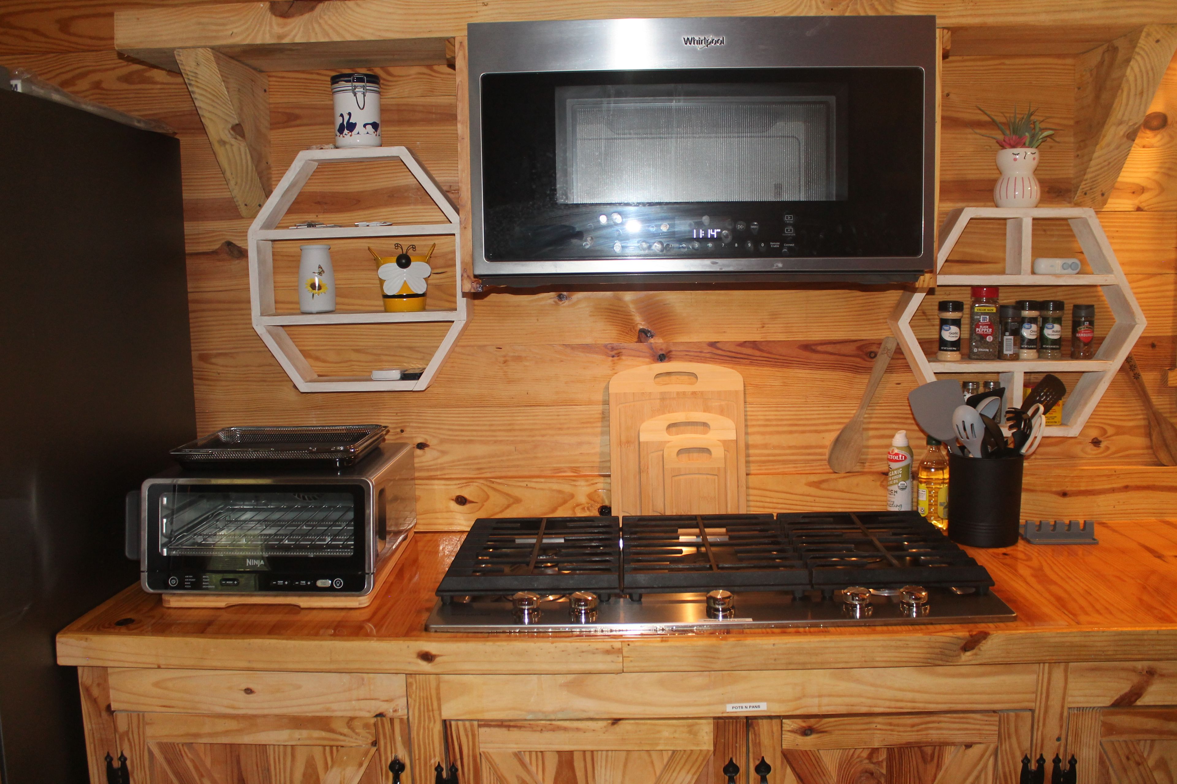 A kitchen with a microwave, oven, and stove. There are wooden shelves with kitchen items and a clock above the stove.
