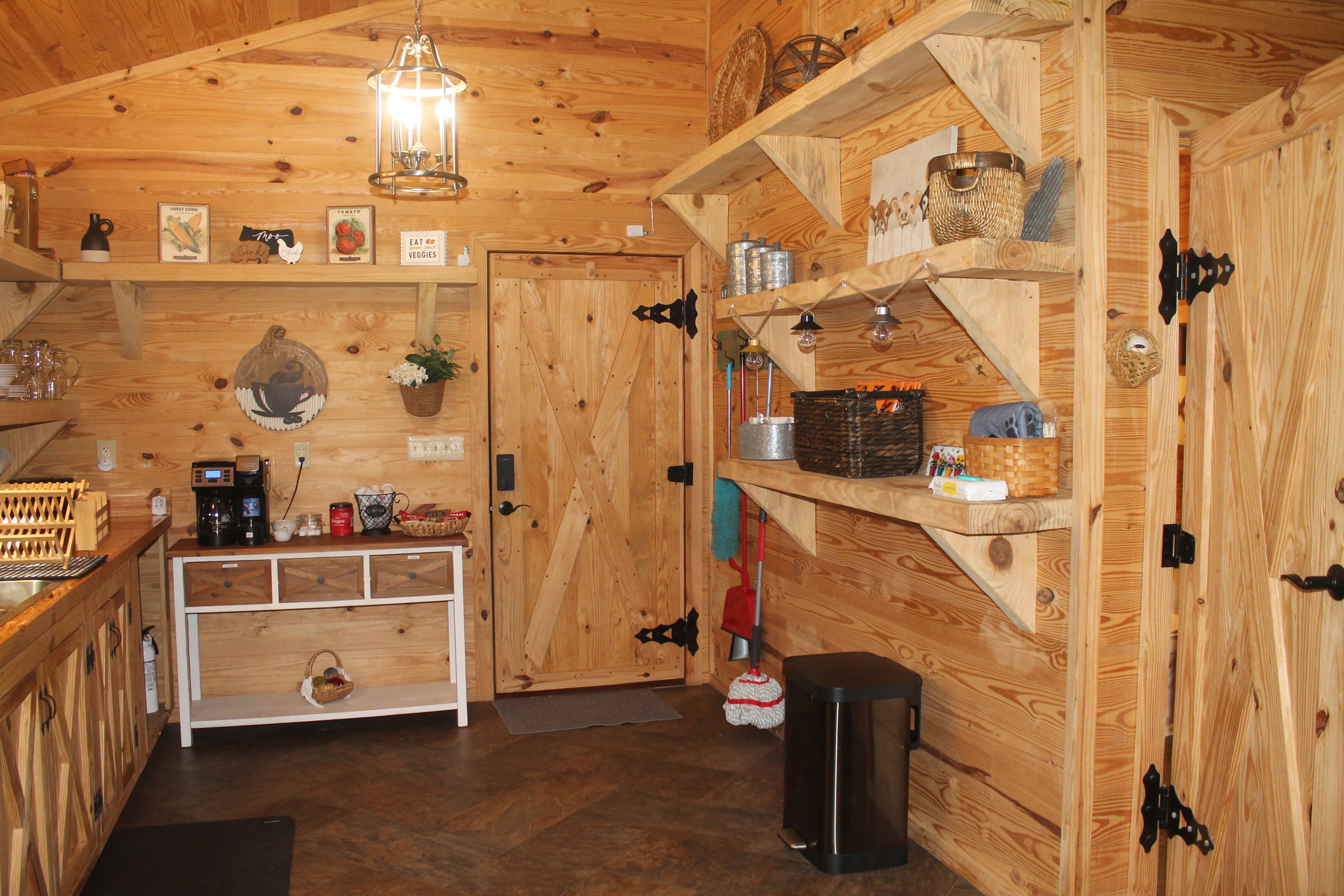 A rustic wooden interior with a kitchen area, wooden shelves, and a hanging light fixture.