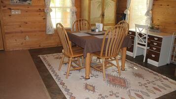 A wooden interior with a dining table, chairs, a cabinet, and a patterned rug.