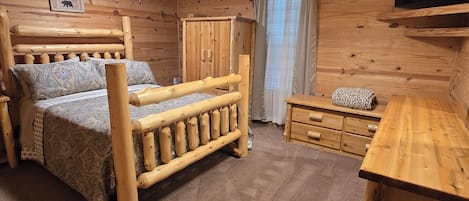 Interior de una cabaña de madera con una cama, un escritorio, un televisor y un ventilador de techo.