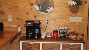 A wooden wall with a coffee machine, a basket of coffee pods, a mug, and a container of Folgers coffee.